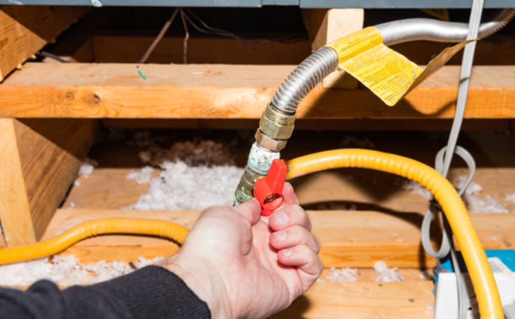 Residential Gas Installation Services and Safety Valve Inspection Gas Installation Services showing a technician turning a red shut-off valve on a flexible gas line in an attic space.