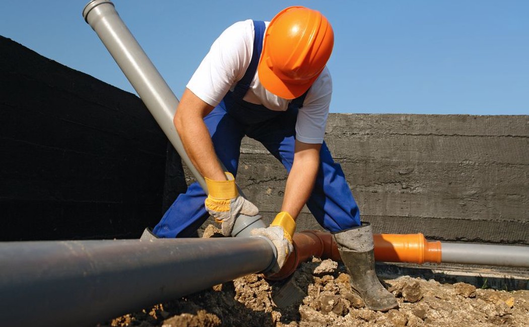 Worker repairing an underground pipe as part of professional Sewer Repair Services to ensure proper drainage.