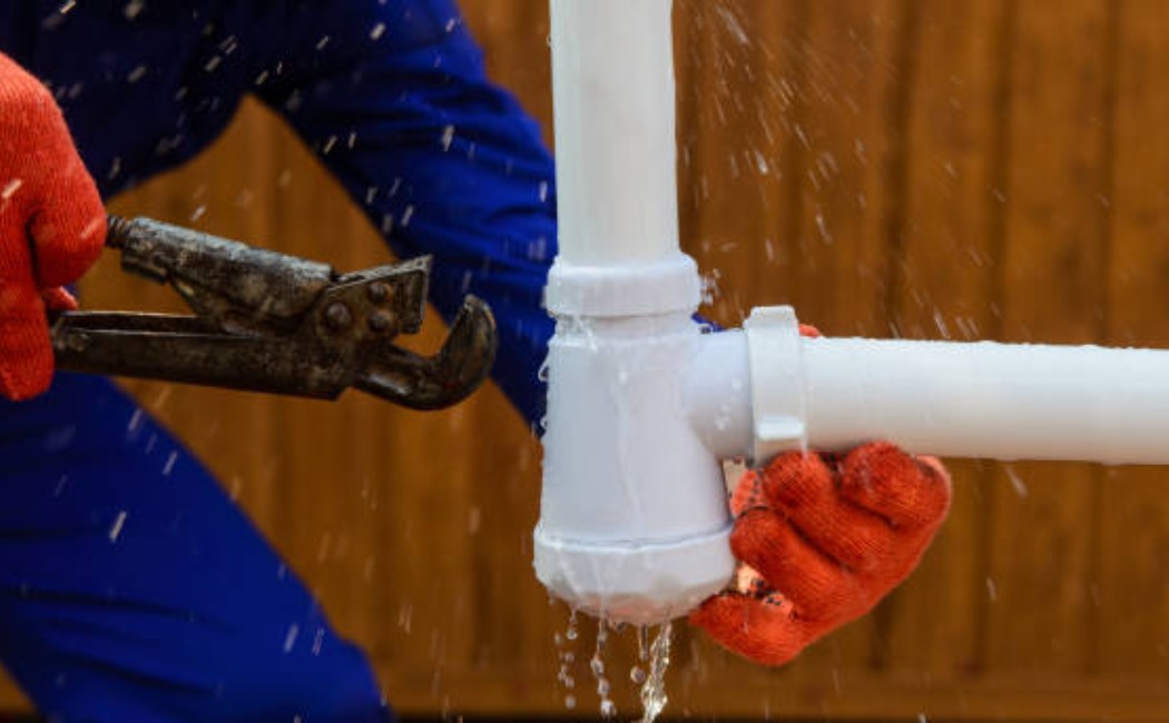 Worker in gloves using a wrench to fix a leaking pipe joint with water spraying, representing reliable leak repair services.
