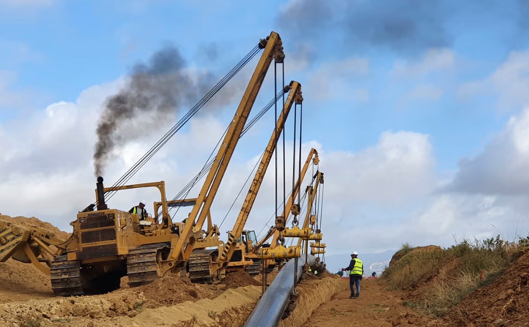 Gas Line Installation with heavy machinery laying a large pipeline in a trench while workers supervise on a construction site.