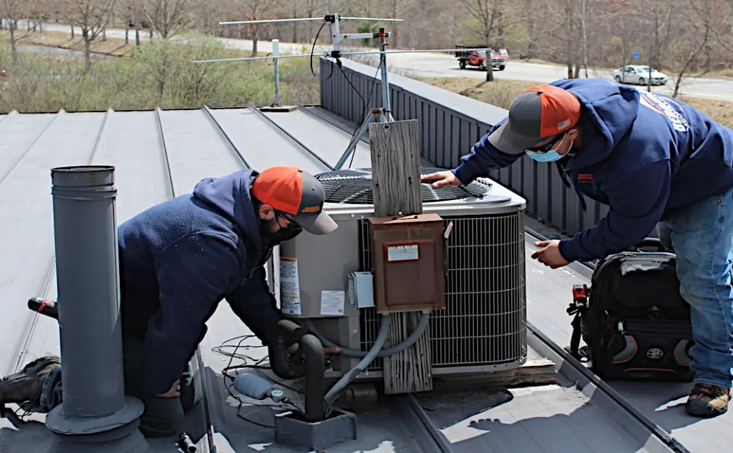 Two technicians performing HVAC Installation Services on a rooftop air conditioning unit while inspecting and adjusting components.
