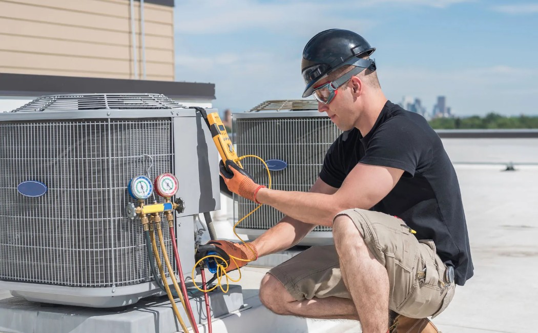 Technician performing HVAC Installation Services on a rooftop air conditioning unit using diagnostic tools and gauges. 