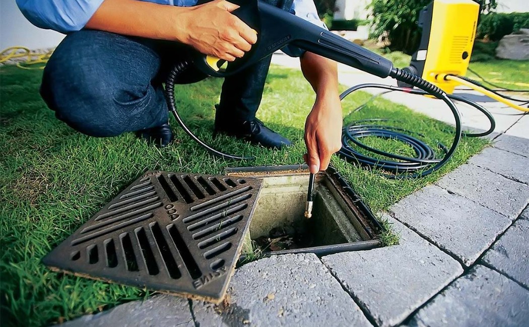 Person using a pressure washer hose for drain cleaning in an outdoor yard storm drain.