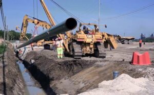 Workers using heavy machinery to lower a large pipeline into a trench during Gas Line Installation at an outdoor construction site.