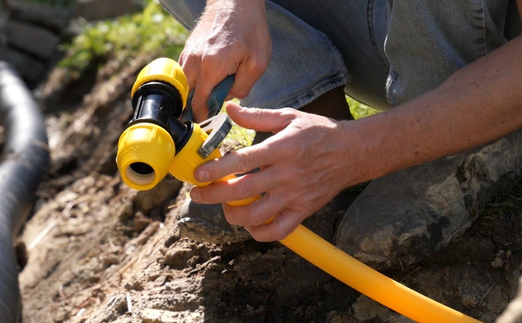 Worker connecting a flexible gas pipe with a fitting tool during Gas Line Installation in an outdoor trench.