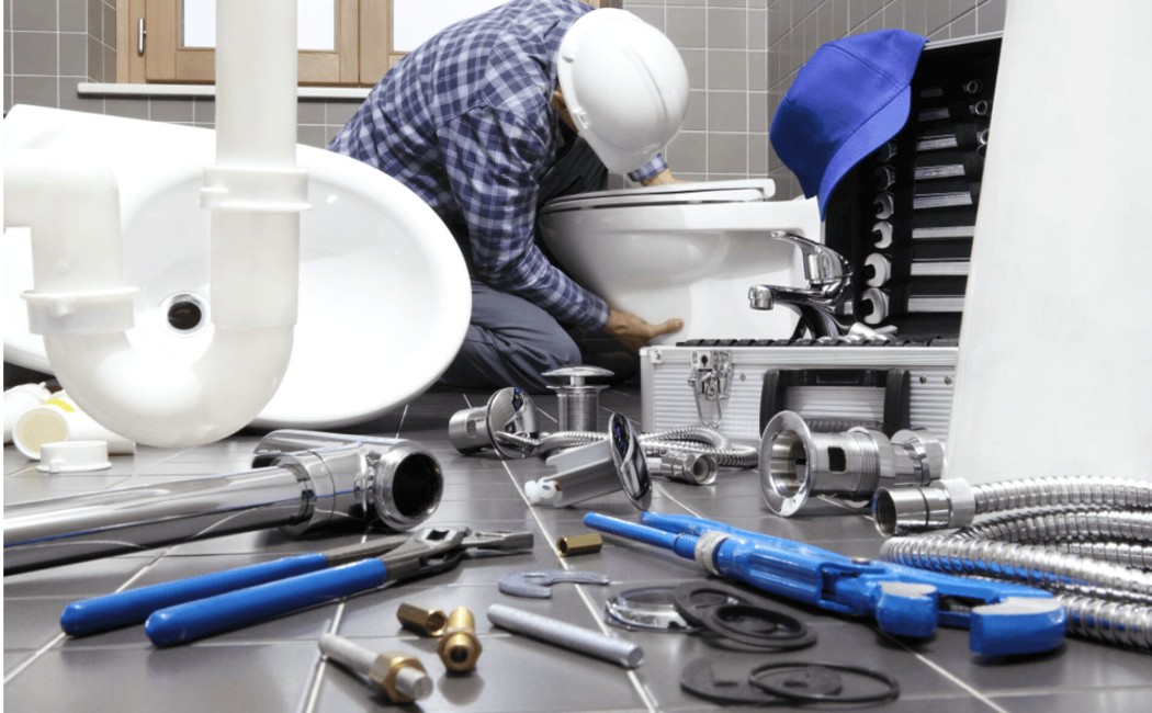 Expert Toilet Installation & Repair for Efficient Bathroom Plumbing Services Plumber installing and repairing a toilet with tools and pipes scattered, representing professional Bathroom Plumbing Services for efficient home maintenance.