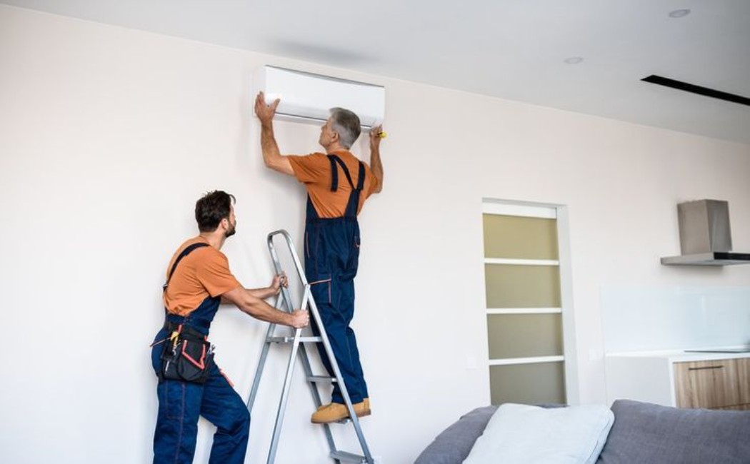 Worker on a ladder installing a wall AC unit indoors. Worker on a ladder performing Air Conditioner Installation by mounting a wall unit inside a modern home.