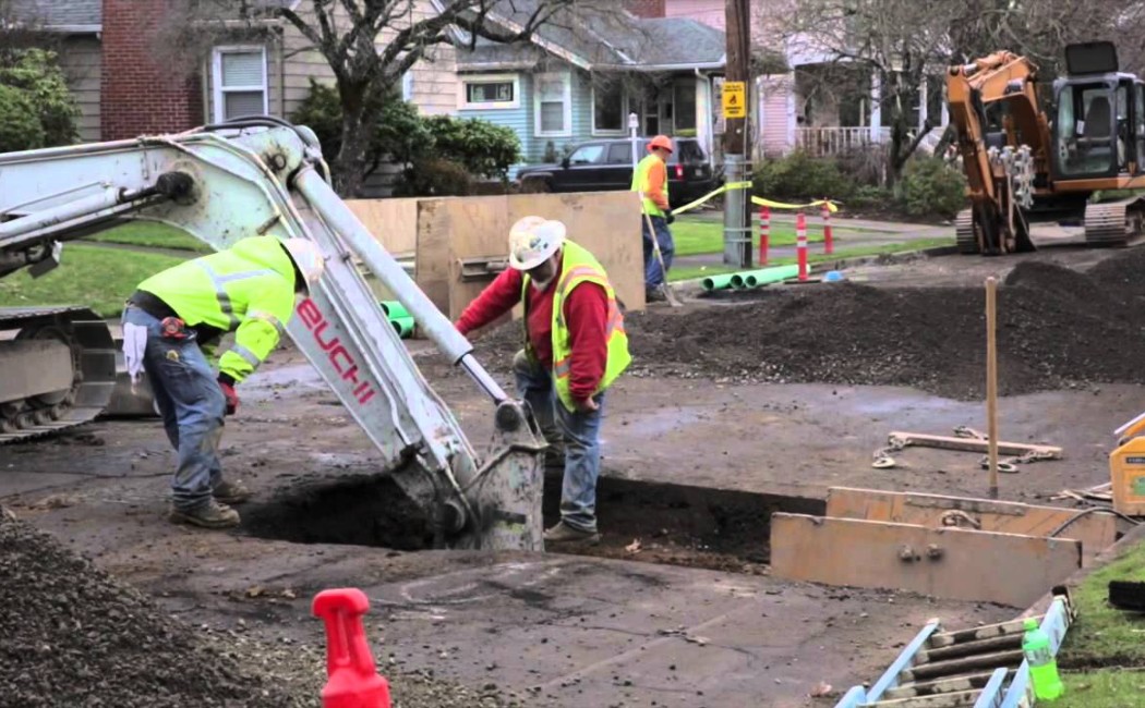 Construction crew performing Sewer Repair Services with excavators and trench-digging equipment on a residential street during underground pipe maintenance work.