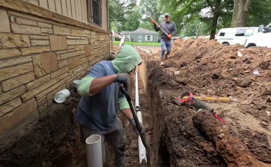 Technicians performing Sewer Repair Services by installing and repairing underground sewer lines beside a residential building.