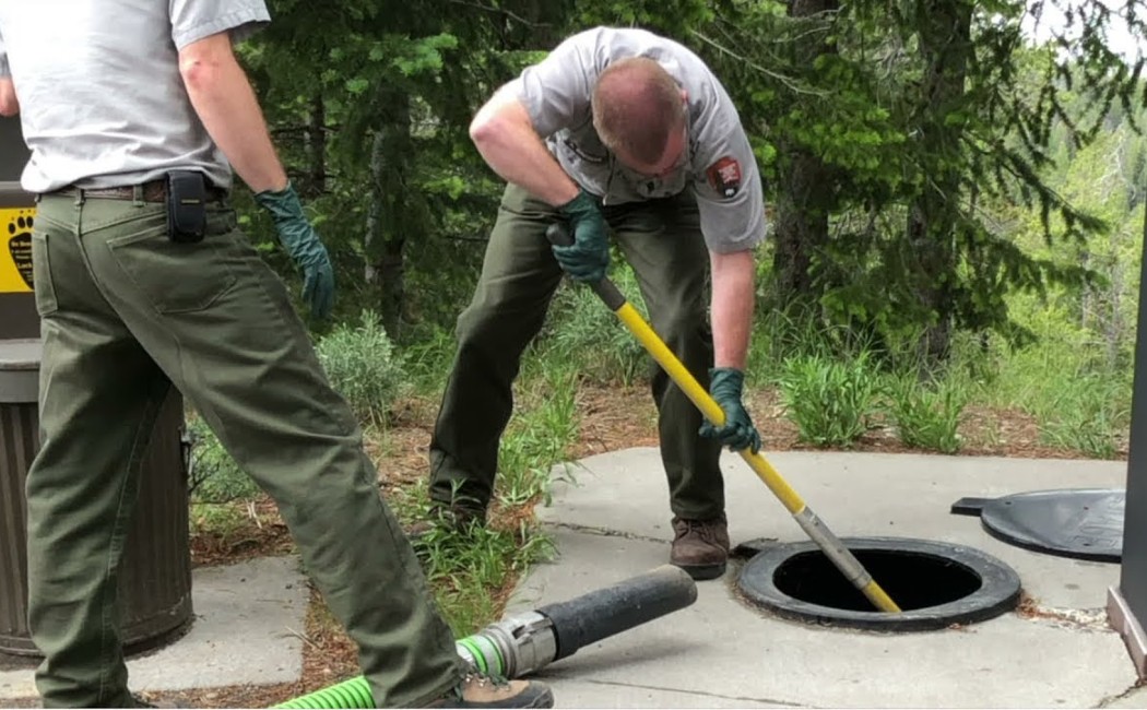 Workers performing Sewer Repair Services by inspecting and maintaining an underground sewer access point outdoors.
