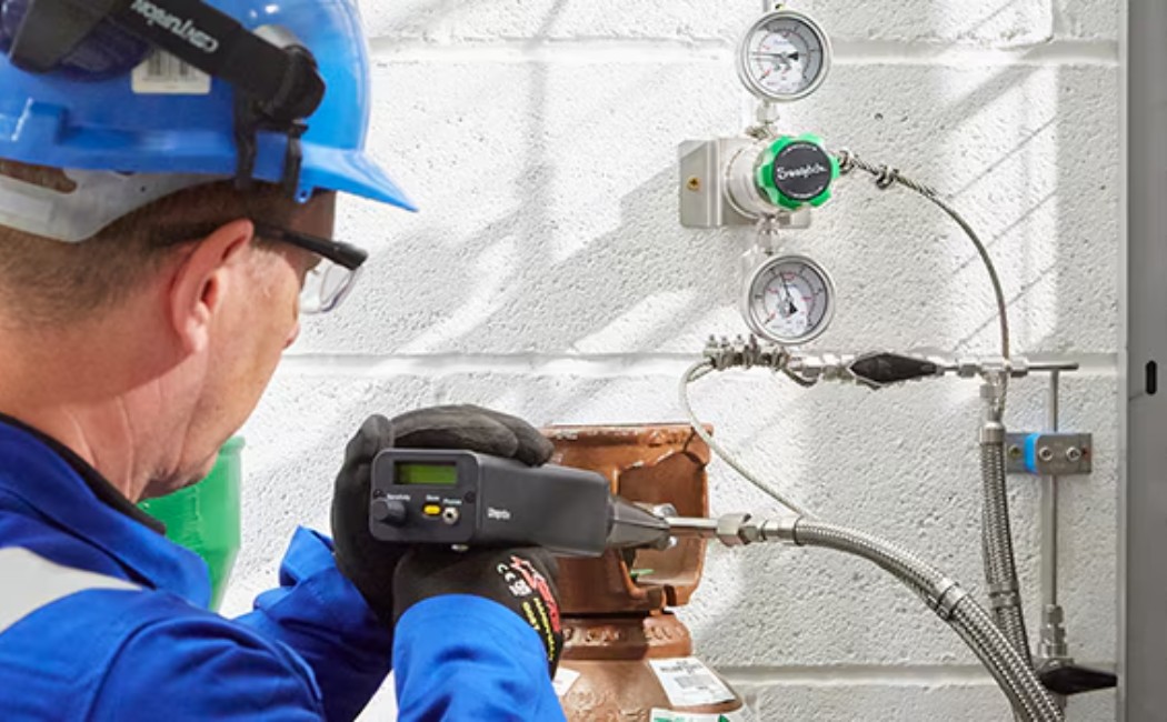 Worker using specialized equipment on a wall pipe system to perform Leak Detection Services.