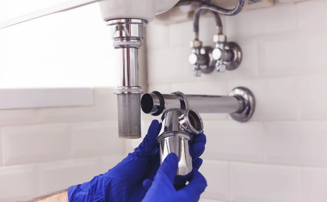Bathroom Sink Drain Pipe Repair Services Plumber installing and repairing sink drain pipes under a bathroom sink with chrome plumbing fixtures.