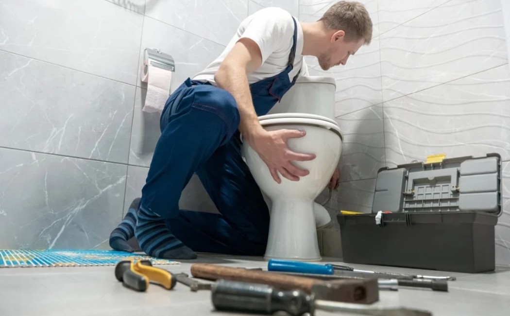 Professional plumber repairing and installing a toilet in a modern bathroom with plumbing tools on the floor.