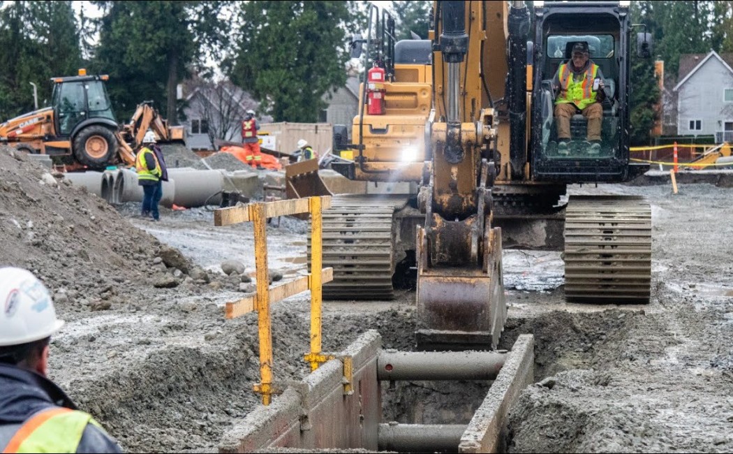 Sewer Installation in progress with construction workers and excavators placing underground pipeline infrastructure at a large excavation site.